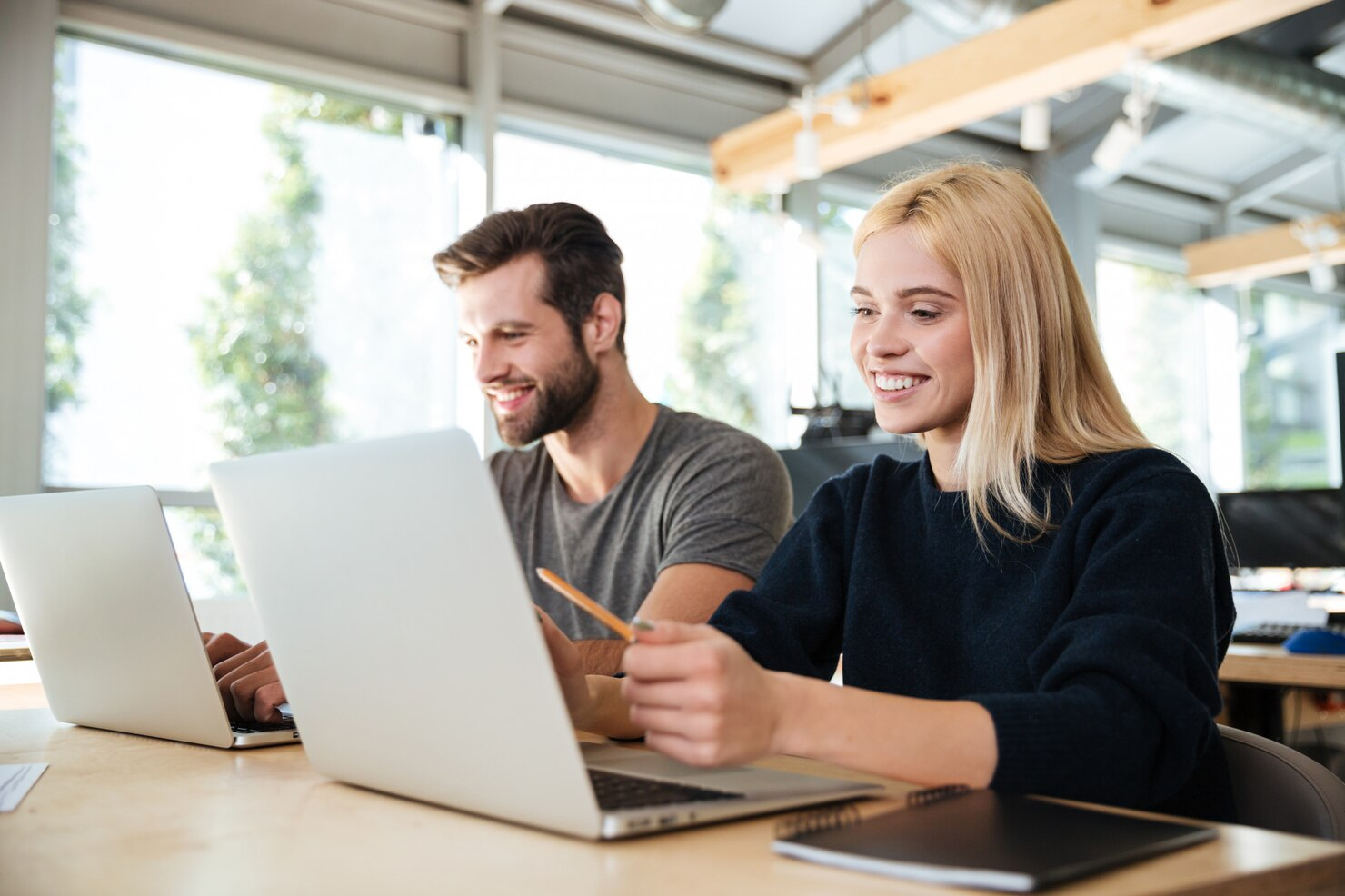 A young man and a young woman seated and working side by side on their open laptops.